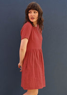Model wears a 100% cotton dress with pockets in a peachy terracotta colour. 