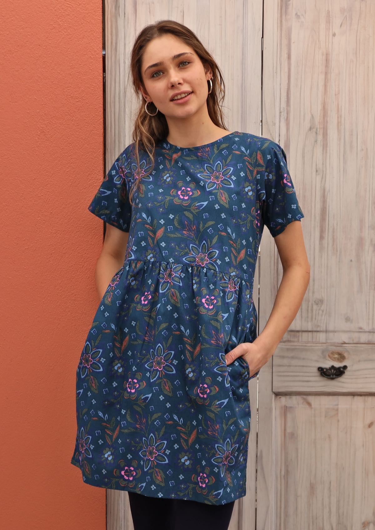 Model layers blue cotton dress featuring empire waistline with black leggings. 