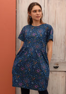 Model wears a 100% cotton short sleeve dress with green, orange and pink florals on a blue base. 