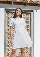 Woman wearing a white cotton sundress standing in front of a textured wall.