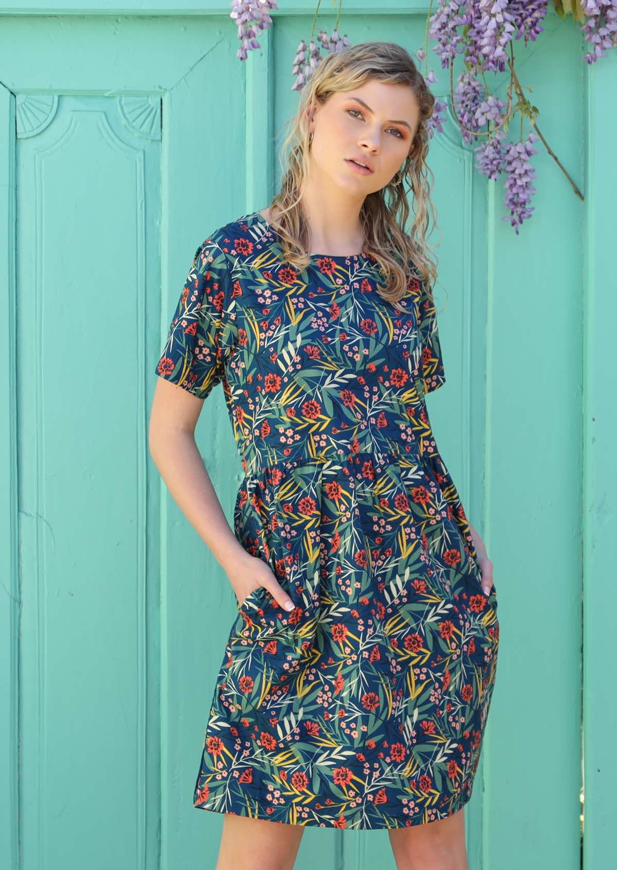 Model wears a 100% cotton dress with a floral print on a blue base. 