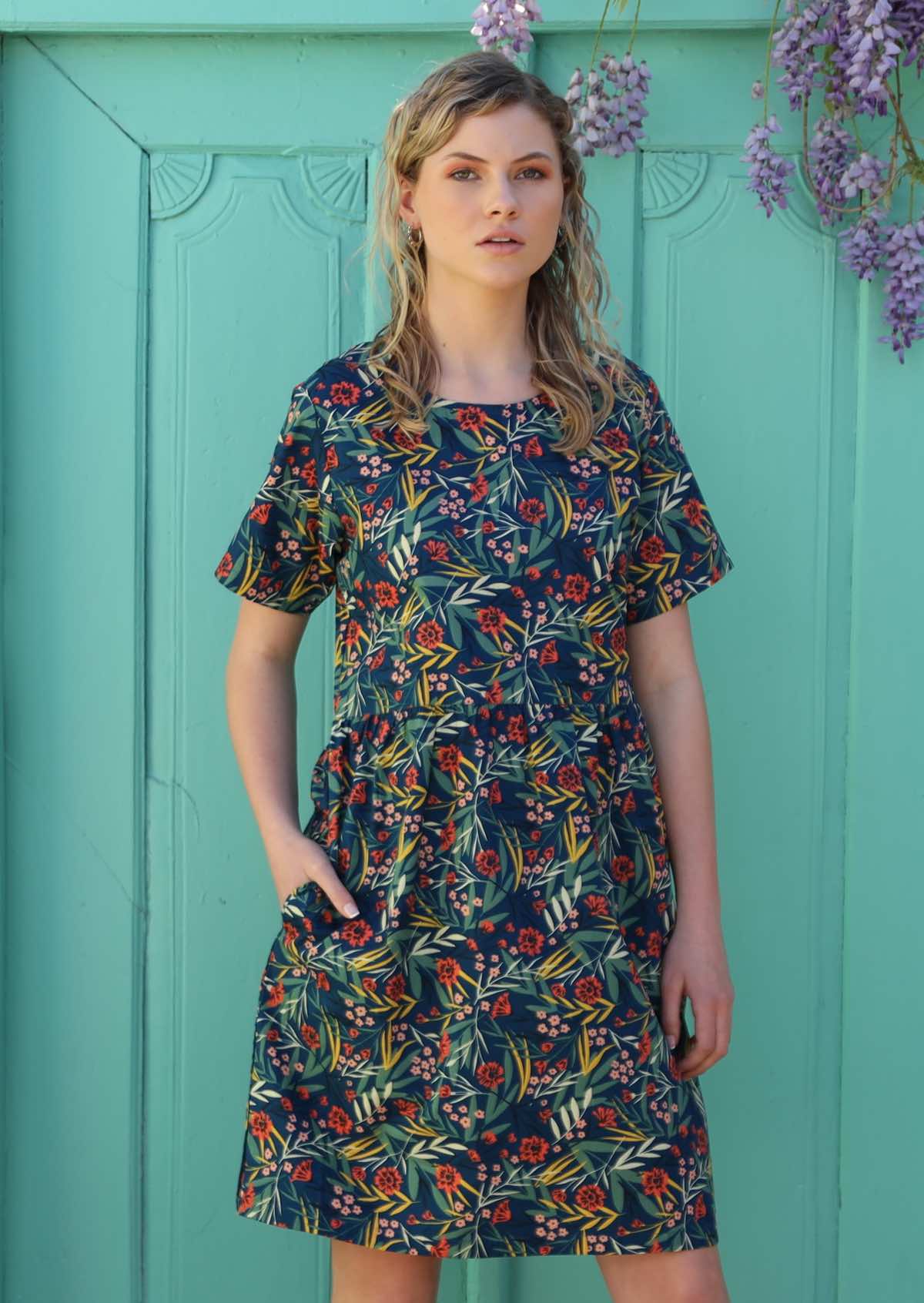 Model stands with her hand in the pocket of her floral dress. 