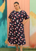 plus size model wears below knee navy blue cotton dress with fun print, sleeves, and pockets
