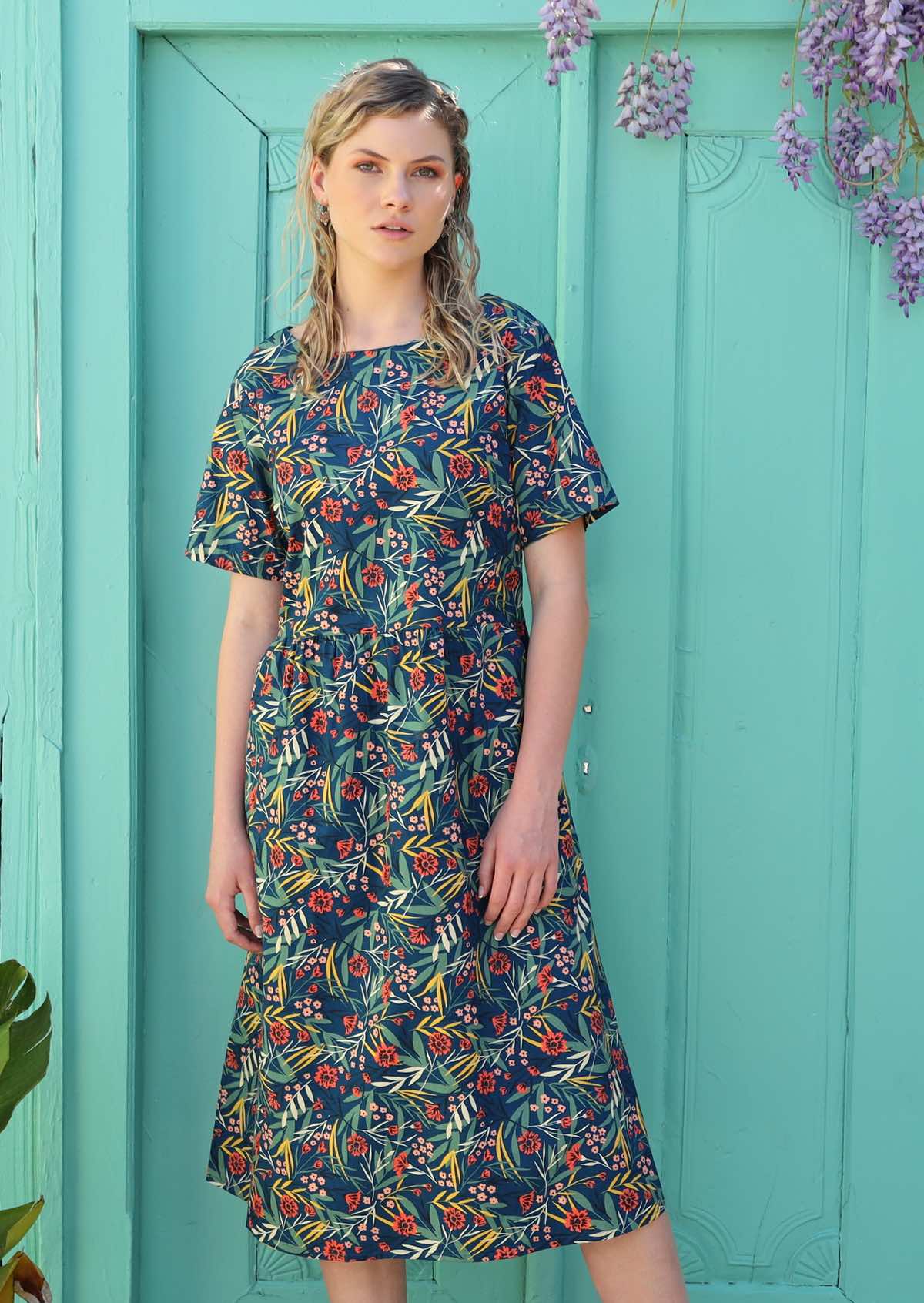 Blonde woman wears a floral dress that sits below the knee. 