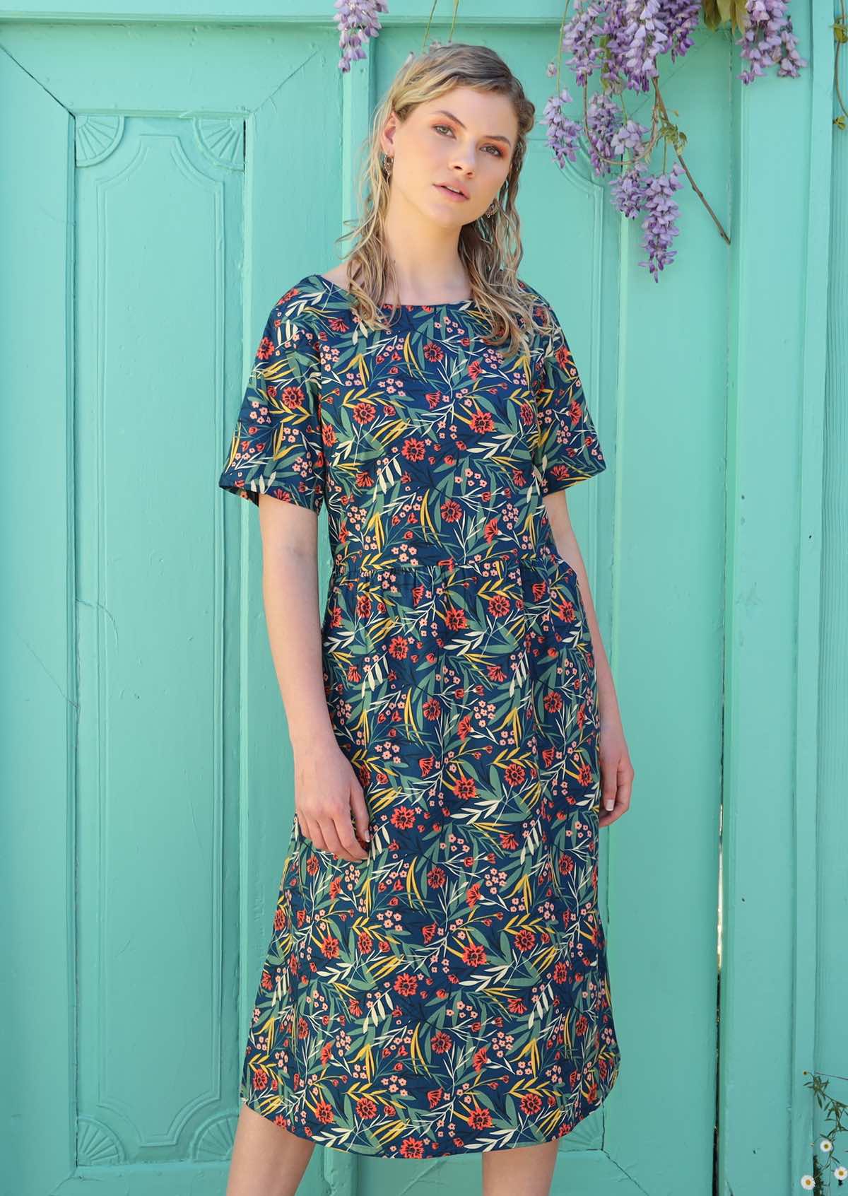 Model wears a loose fitting dress with a loose empire waistline with small pin tucks. 