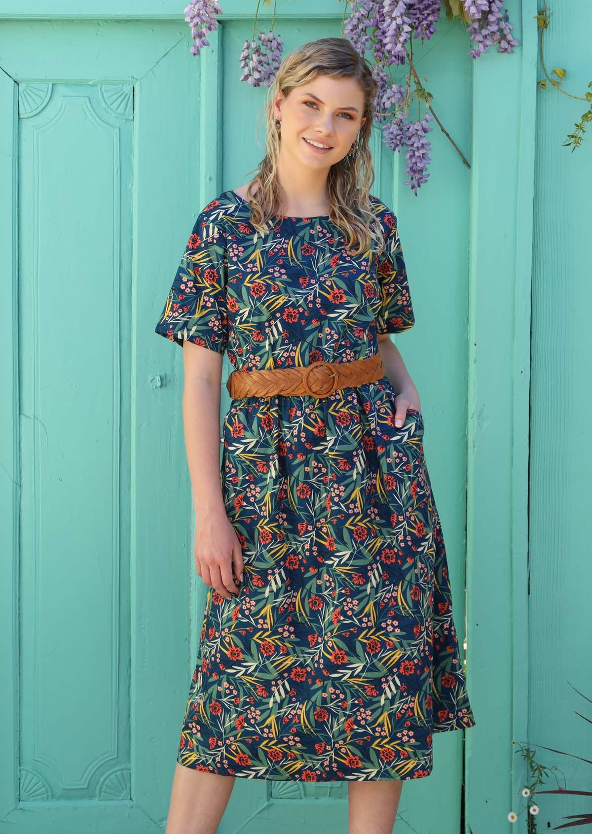 Blonde woman wears a dress with pockets that is styled with a belt at the waist. 