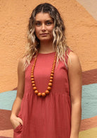 Woman in pink dress with long chunky wood bead necklace tan coloured