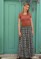 Model pairs three tiered skirt with a belt, short sleeve top and sandals. 