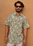 Man poses in short sleeve relaxed fit cotton collared shirt with one breast pocket in pale green based floral print.