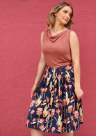 Woman wearing a pink top and button through knee length cotton floral skirt with box pleats and belt loops