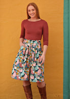 Woman wearing a cotton knee length button through A-line skirt with box pleats, with hand in pocket