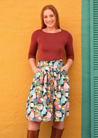 Woman wearing a pastel print skirt with belt loops, buttons through the centre, with hands in pockets