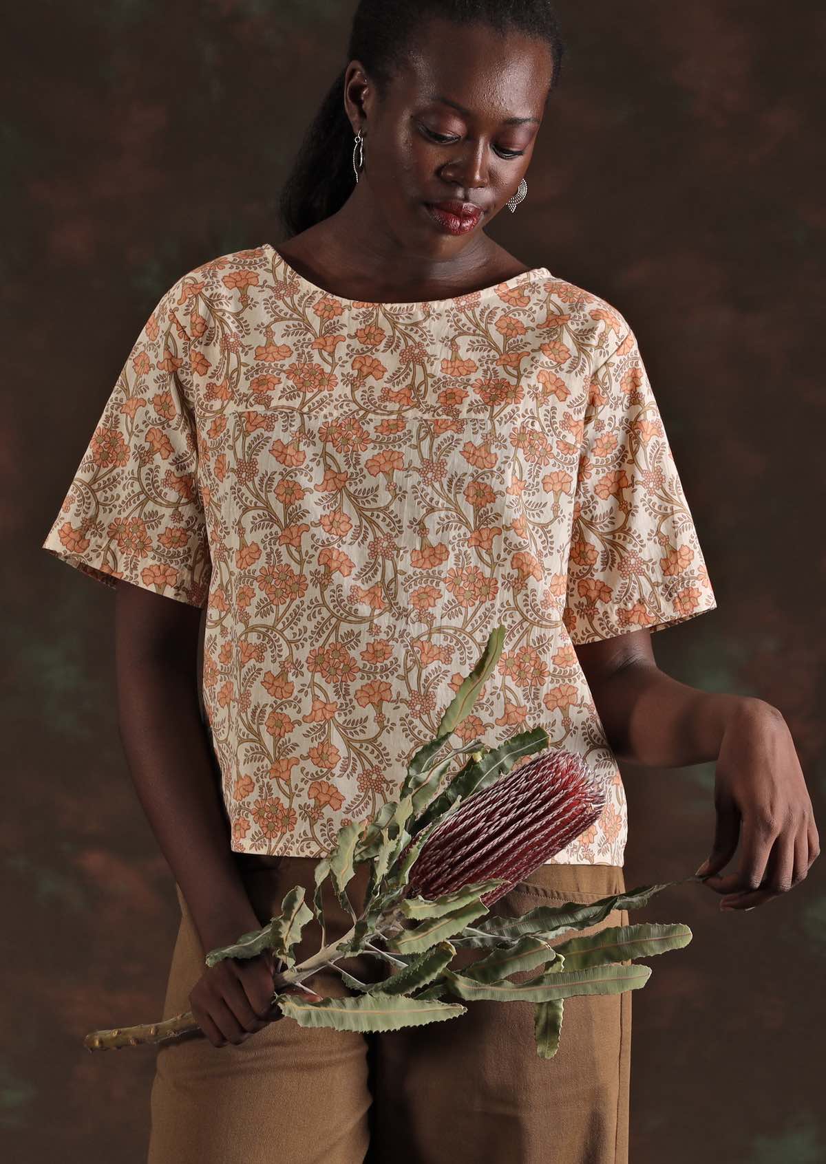 Model wears cotton floral short sleeve top holding a banksia flower