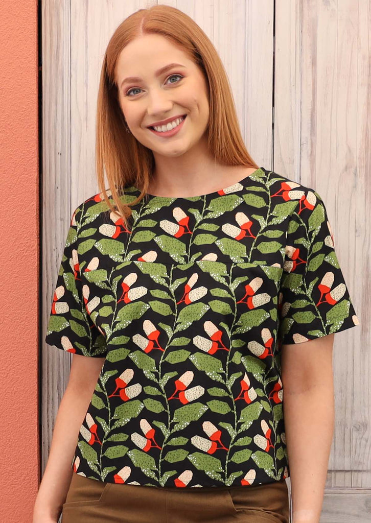 Model wears Neesha Top Oak green orange and white botanical print on black base cotton boxy top with T-shirt sleeves round neck and decorative buttons down back | Karma East Australia