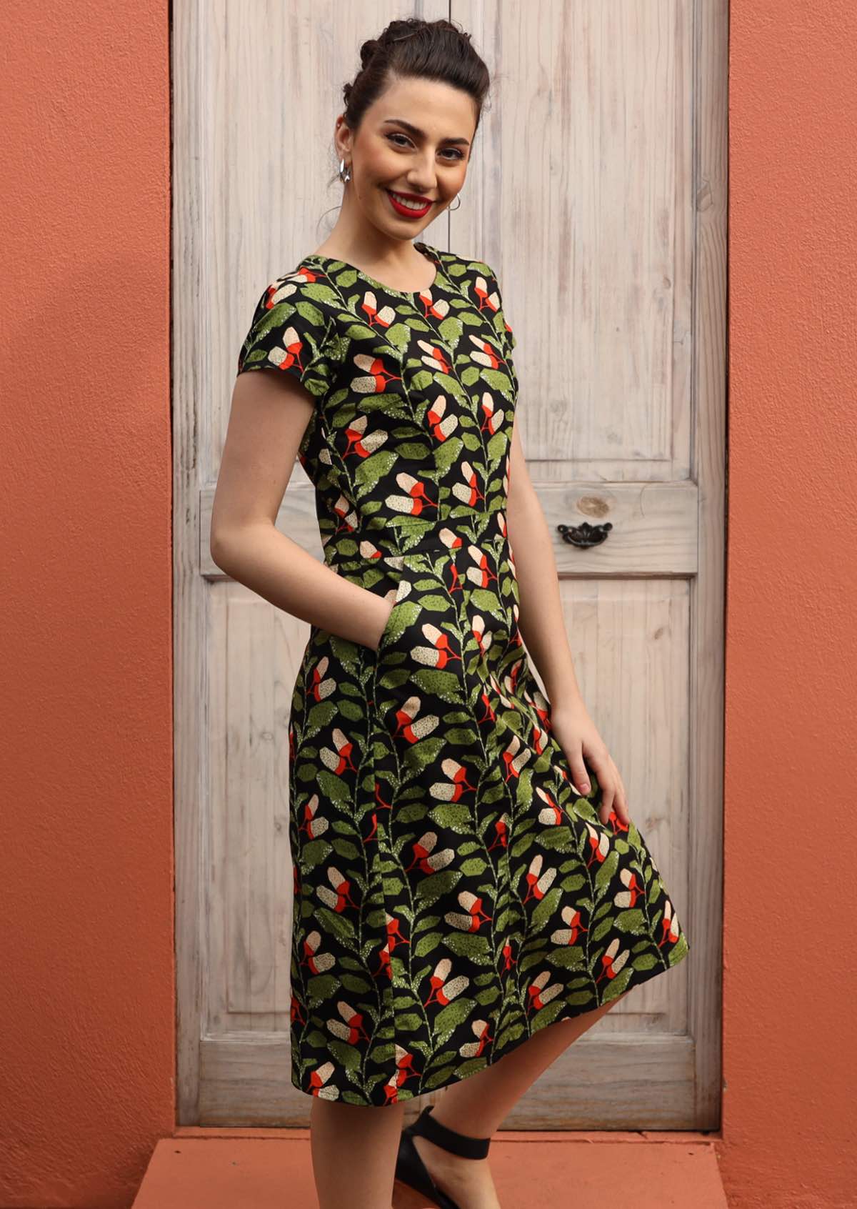 Model wears green orange and white speckled botanical print with black base cotton dress