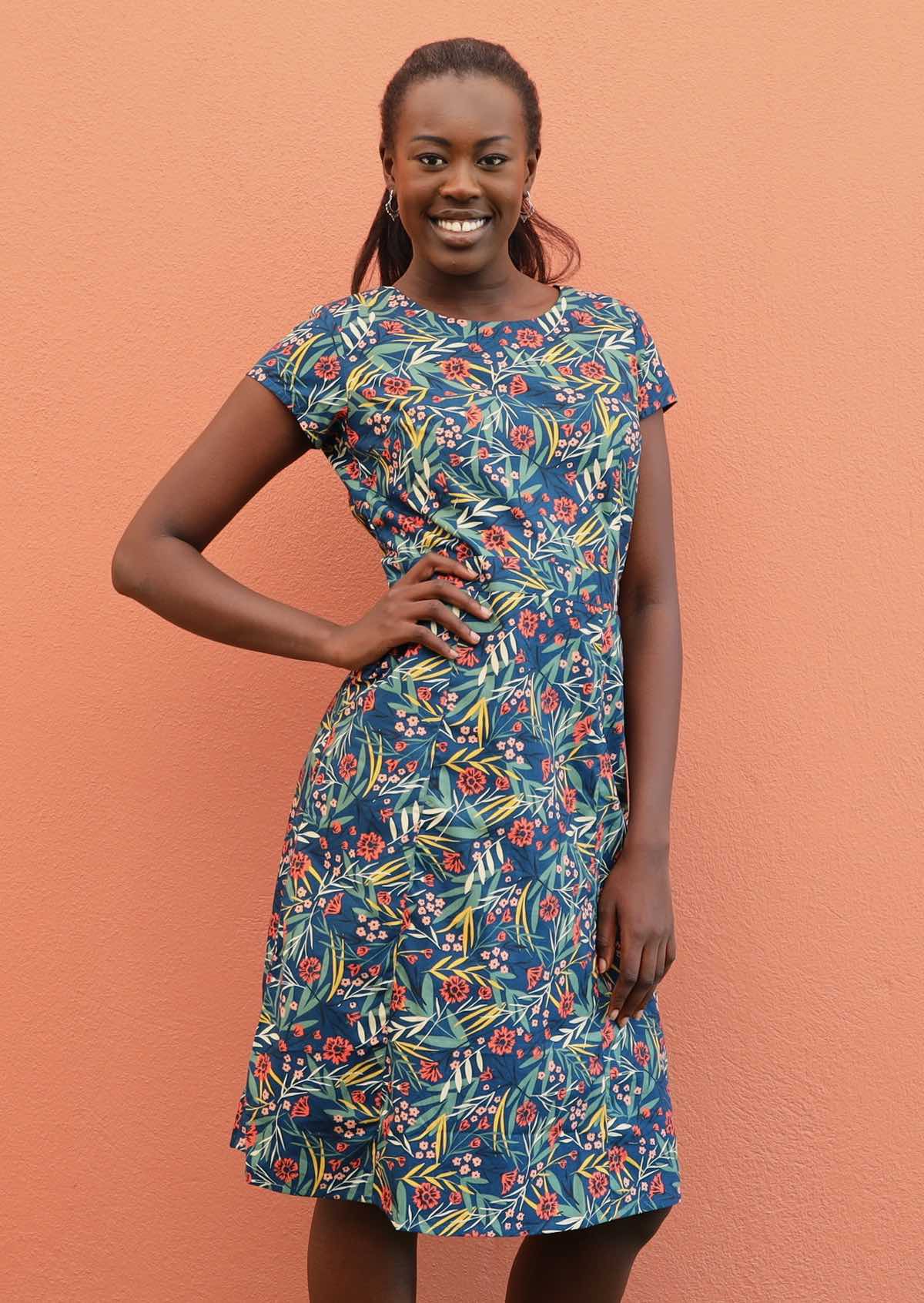 Smiling model wears 100% cotton dress with a round neckline and cap sleeves. 