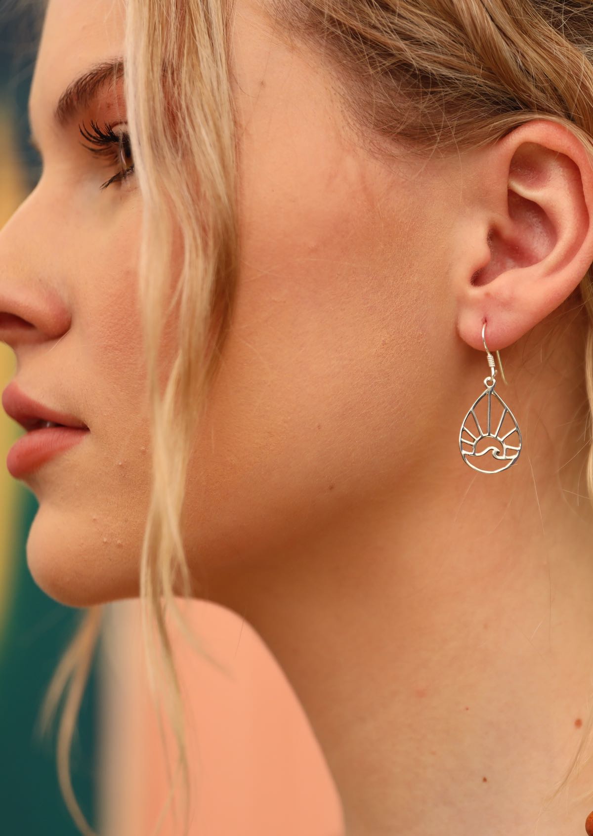 Blonde woman wearing silver earrings that are teardrop shape with a sun and wave within it