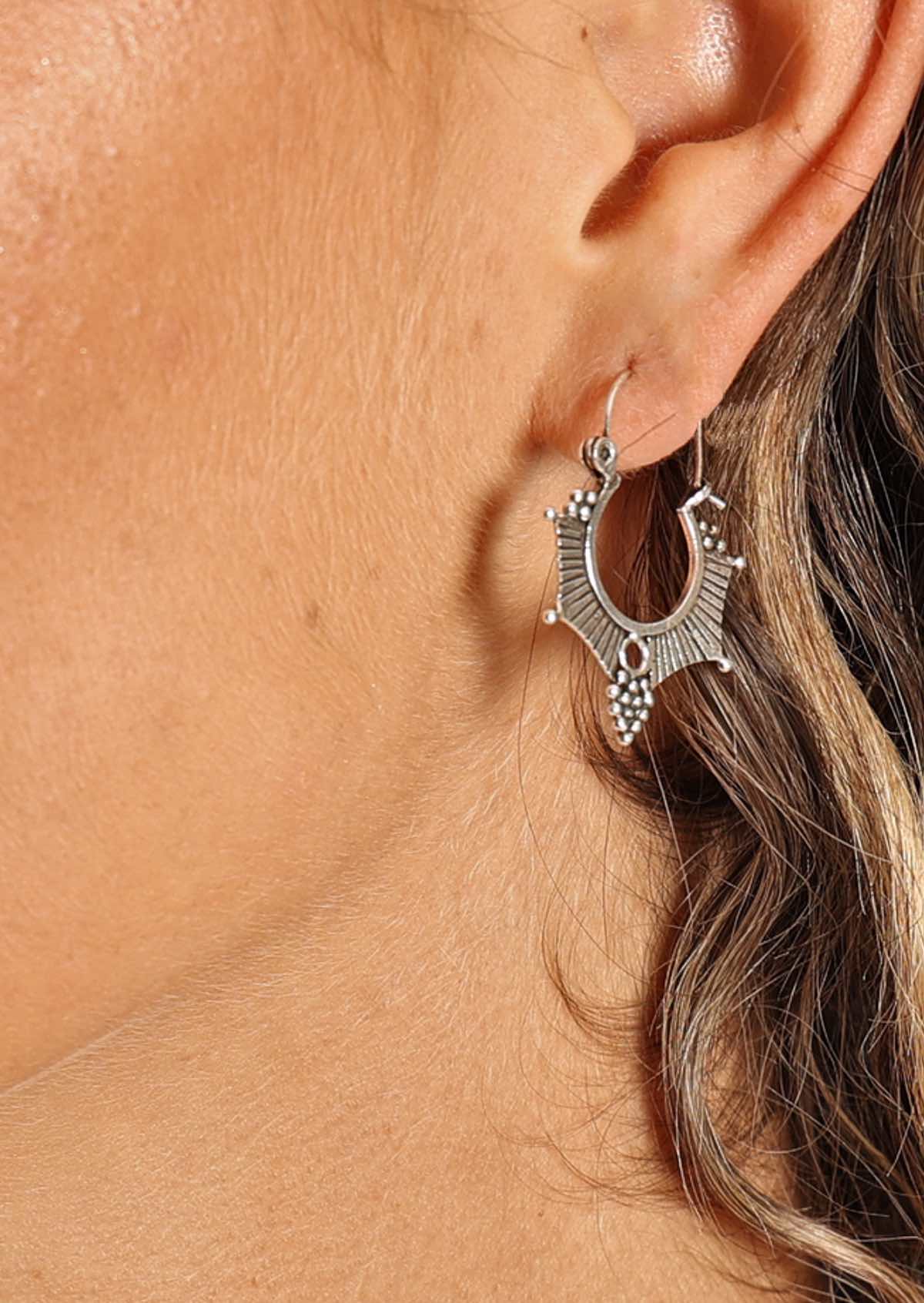 woman's ear wearing large tribal style silver hoop earrings