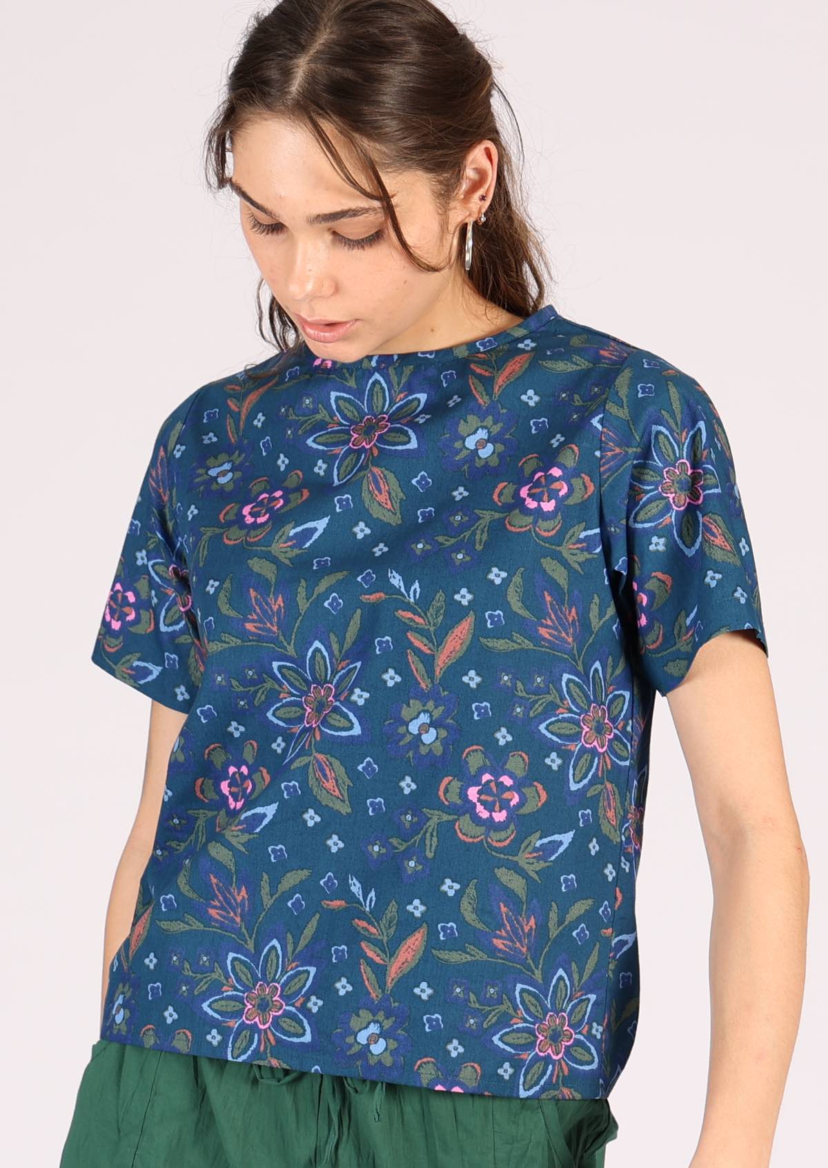 Blue based cotton top has a decorative floral pattern with green, orange and pink. 