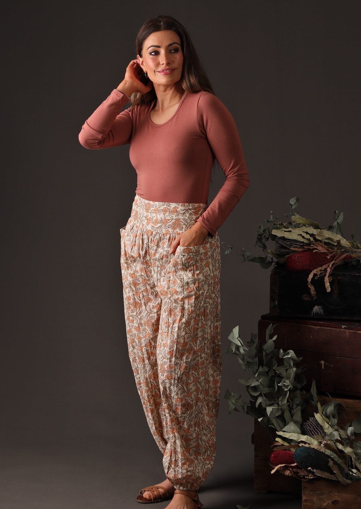 Model wears 100% cotton pants with an elastic waist and ankles. These loose fitting pants have pockets and feature a floral peach and green print on a cream base