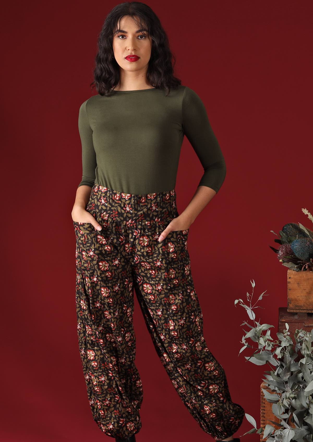 Woman wears pants with a red and olive pattern on a black base