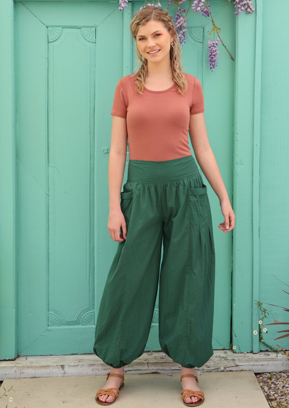 Model pairs loose fitting green pants with elasticated waist and ankles with sandals. 