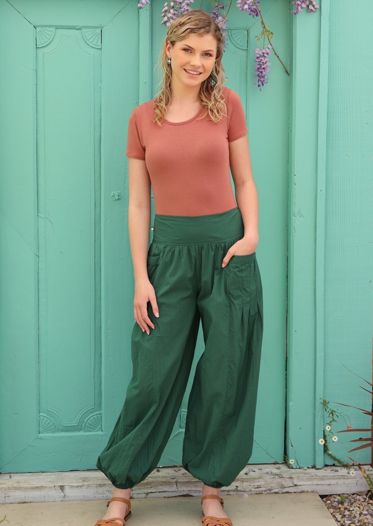 Woman has her hand in the pocket of her green pants with an elasticated waist. 
