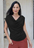 Woman wearing a black sleeveless top with a draped cowl neckline and rust pants