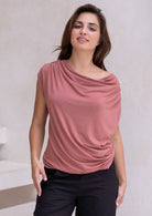 Woman wearing a pink sleeveless top with a draped neckline against a neutral background