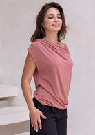 Woman wearing a dusty pink top with a cowl neckline and black pants against a plain background