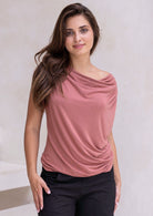 Woman wearing a dusty pink top with a draped neckline against a plain background
