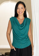 Woman wearing a jade green sleeveless top with a draped neckline, with hand in pocket of pants