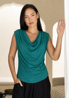 Woman wearing a jade green sleeveless top with a cowl neckline and pleats on each shoulder.