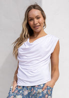 Woman wearing a white sleeveless top with a cowl neckline paired with floral pants against a white background