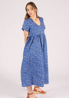 Model wears blue base white floral print cotton midi length button through relaxed fit dress with empire waistline