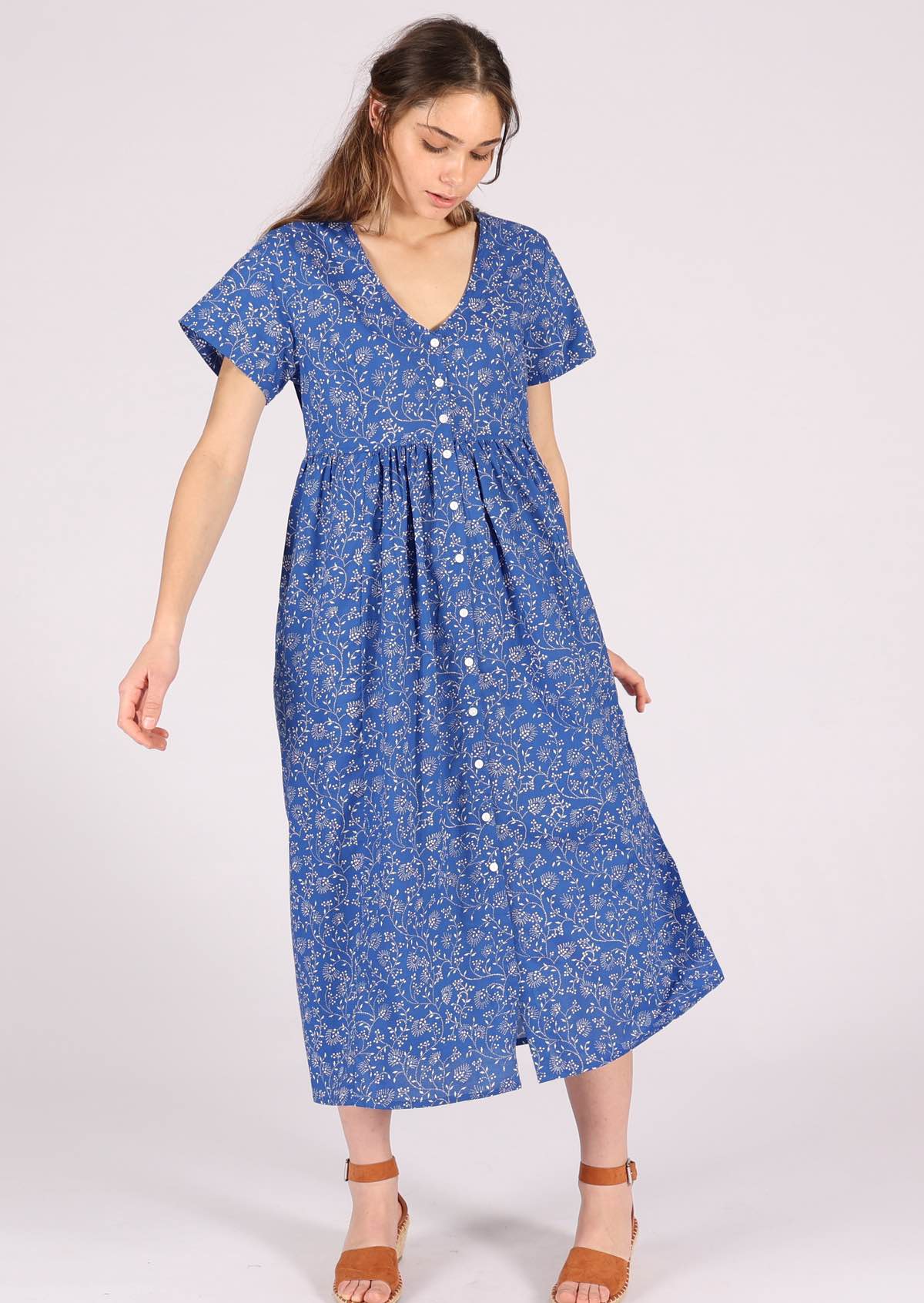 Model wears blue base white floral print cotton midi length button through relaxed fit dress with hidden pockets