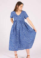 Model wears blue cotton midi length button through relaxed fit dress with V-neck and empire waistlie