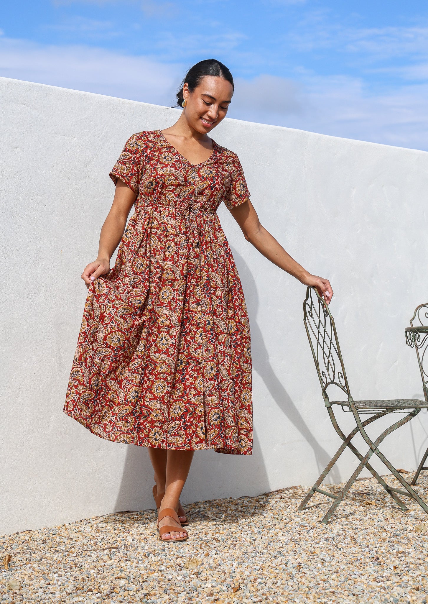 Woman wears lightweight cotton relaxed fit button through red floral dress with  hidden side pocket.