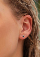 woman's ear with small silver and rainbow coloured stud earrings 