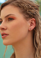 model with blonde hair wearing small silver and rainbow coloured stud earrings 