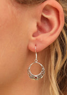92.5% silver hook earrings in the shape of a woven moon with a red diamond shaped gem set at the base on woman's ear