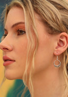 Blonde woman wearing 92.5% silver earrings in the shape of a woven moon with a red diamond shaped gem set at the base.