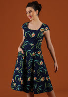 Woman wears a navy dress with a green floral pattern. 