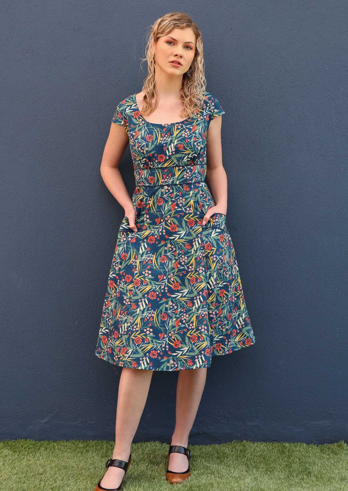 Model stands with her hands in the pockets of her retro style dress. 