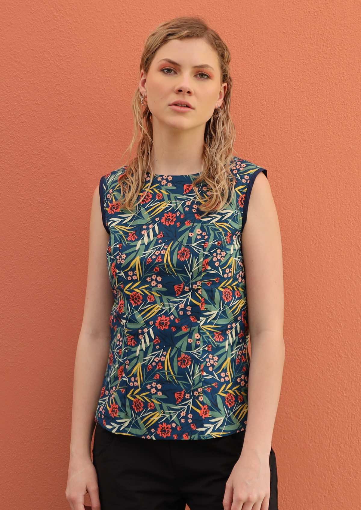 Blonde woman wears a colourful floral top with a blue base. 