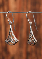 92.5% silver dangling earrings with a triskele on a wire for display.
