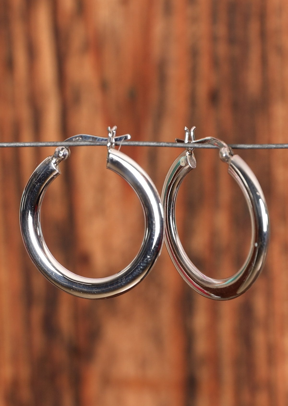 92.5% silver broad hoop earrings placed on a wire for display.