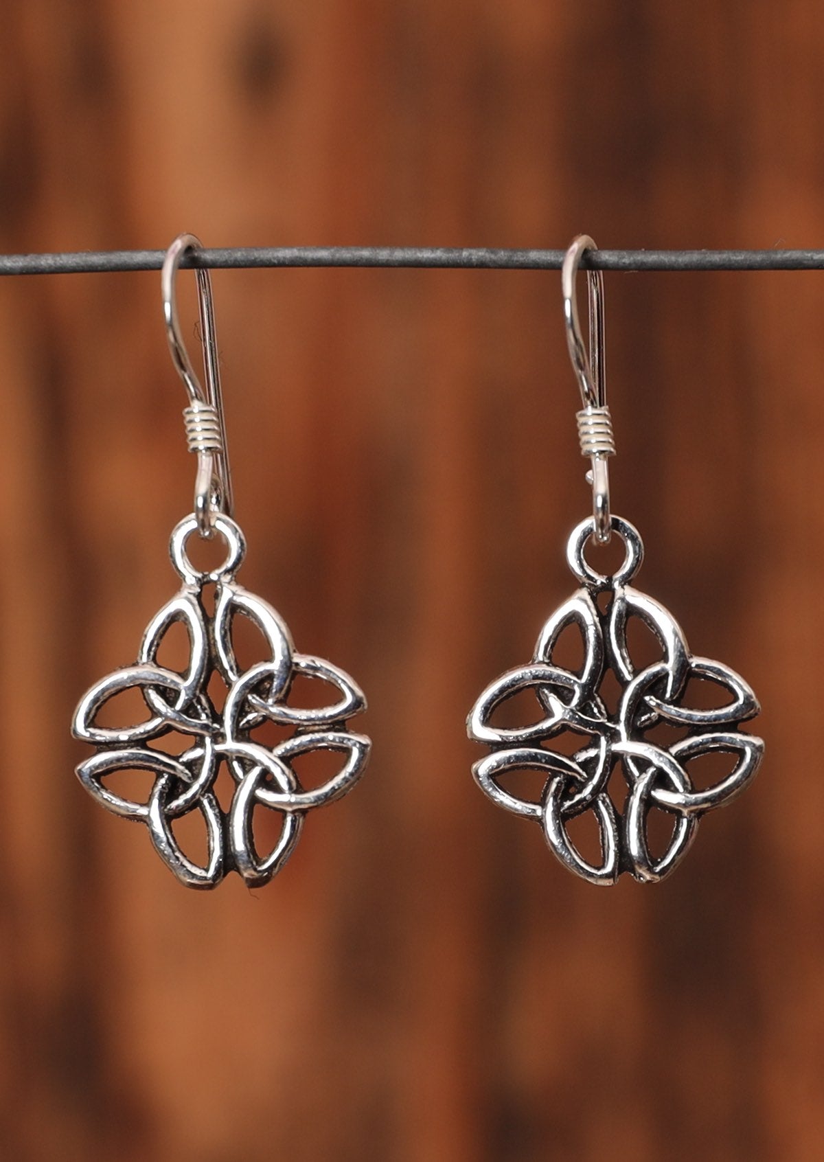 92.5% silver Celtic clover earrings sit on a wire for display.