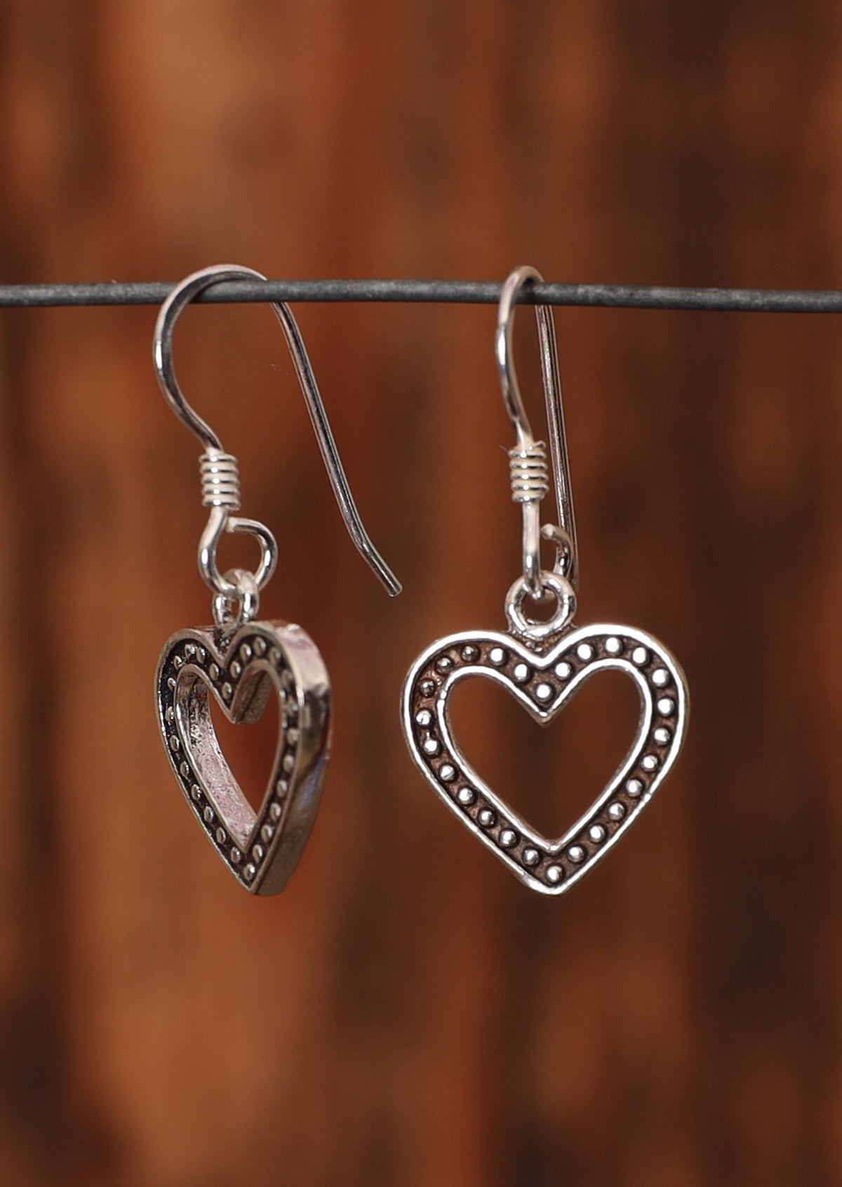92.5% silver heart shaped earrings sit on a wire for display.
