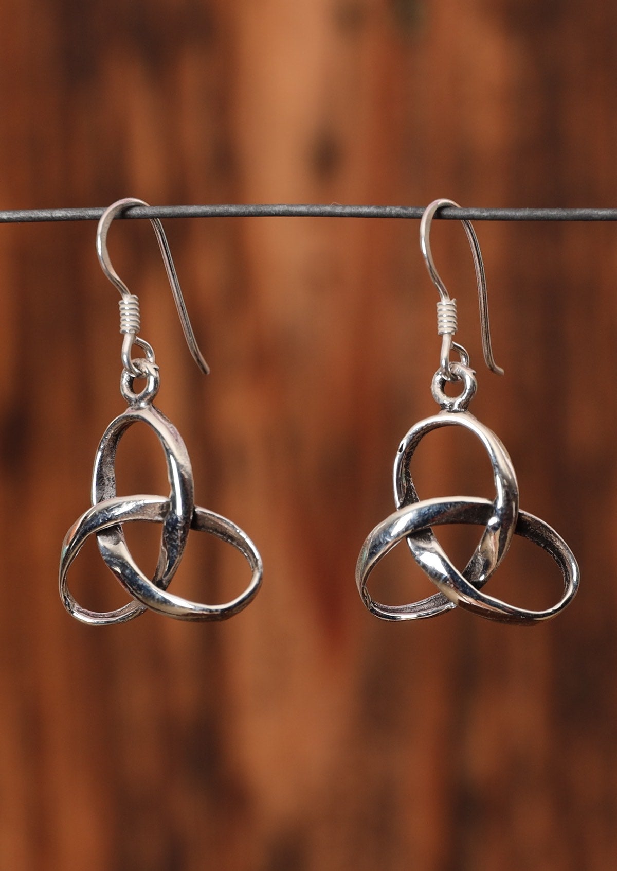 92.5% silver continuous knot earrings hanging on a wire for display.